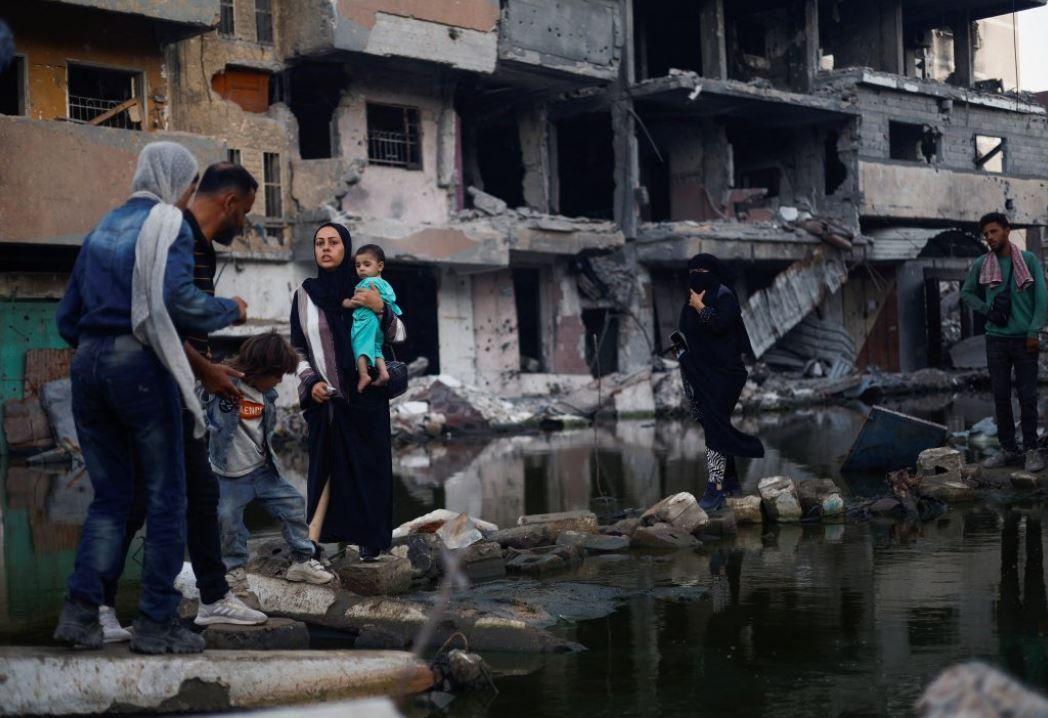 غزيون يقفون قرب مبانٍ دمرتها غارة إسرائيلية في خان يونس