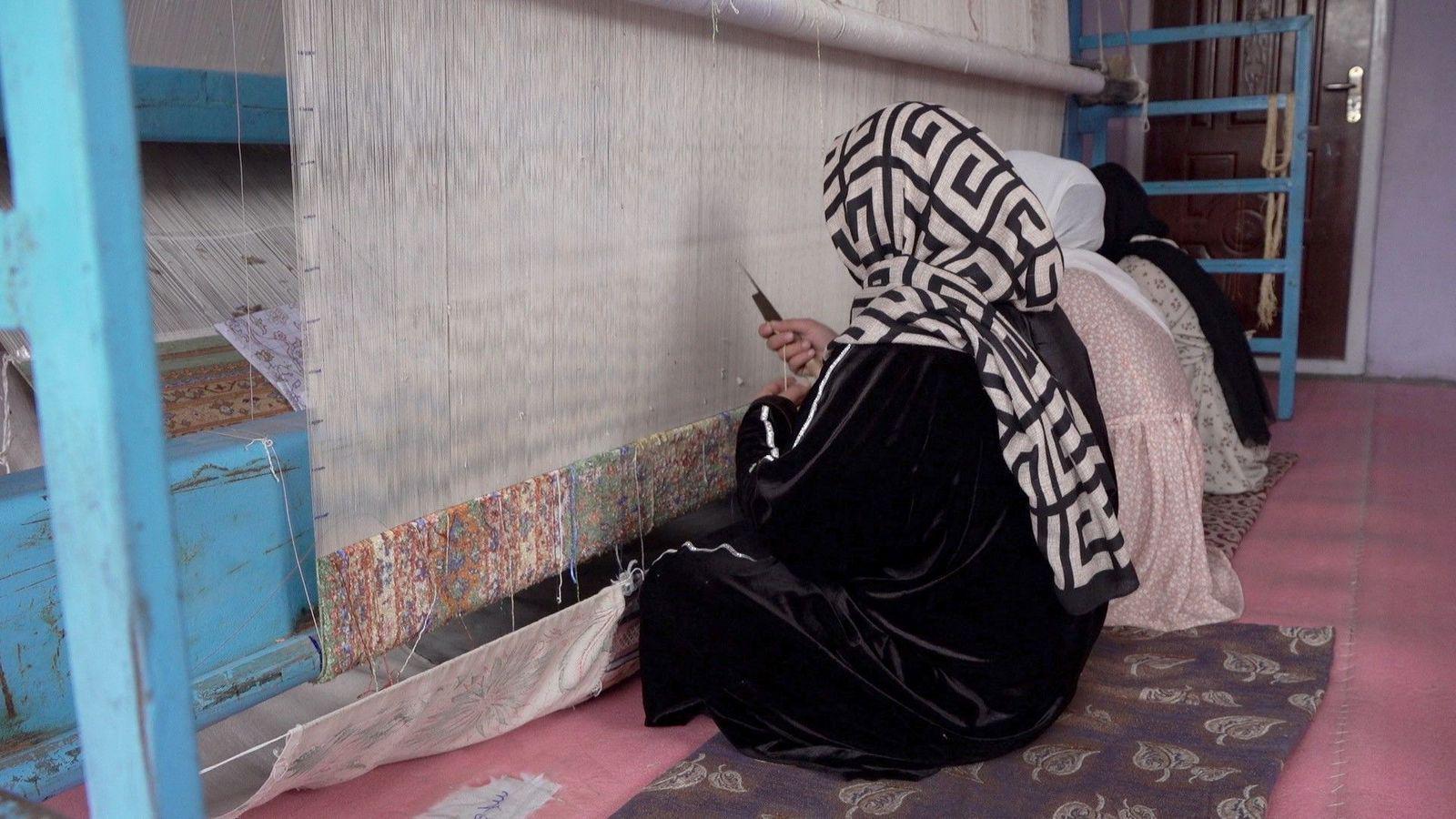 ثلاث نساء يجلسن على الأرض أمام أحد الأنوال، لصناعة سجادة كبيرة 