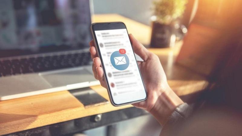 يد تمسك بهاتف جوال وتفتح فيه رسائل بريداً إلكترونيا 