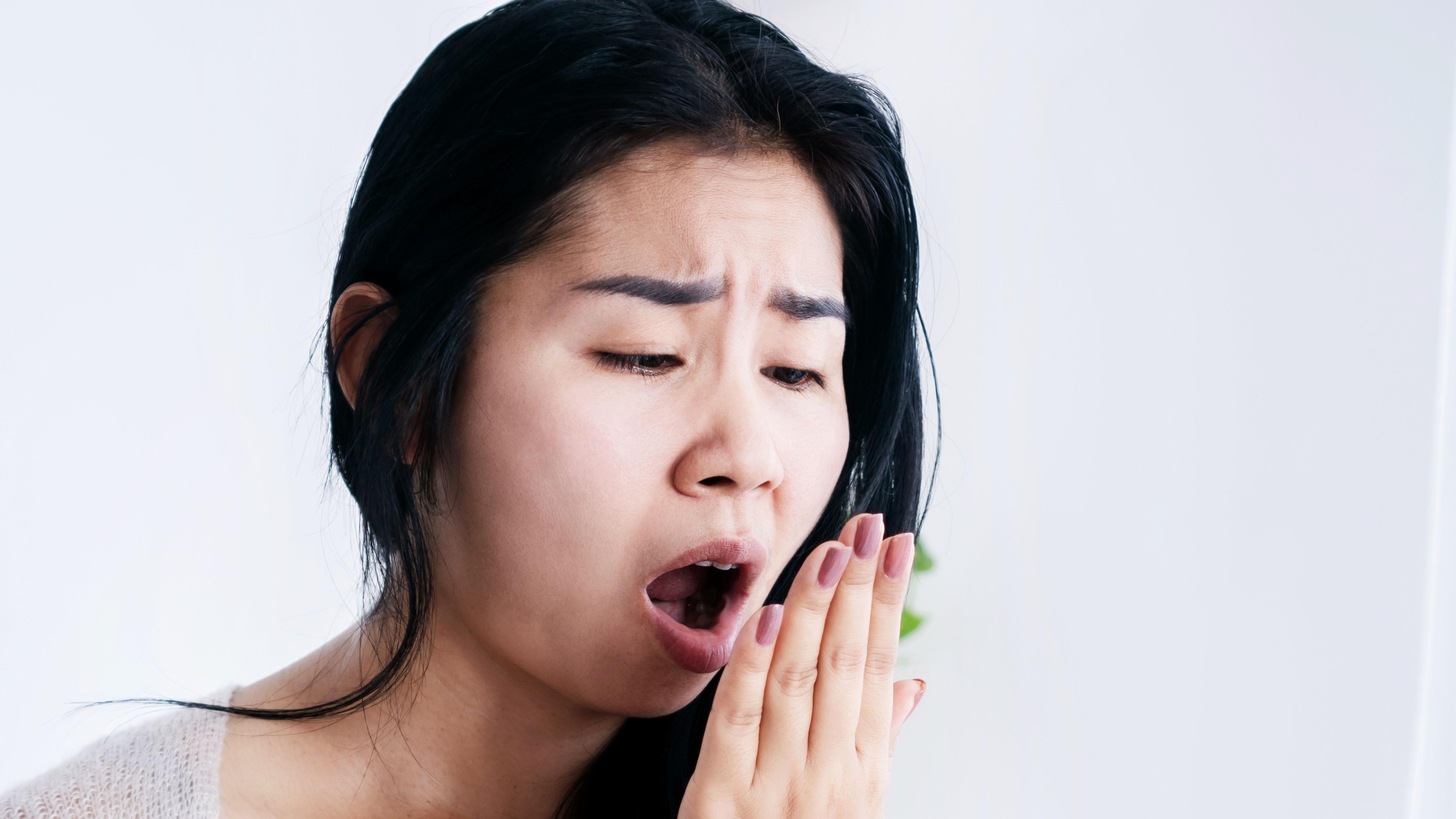 امرأة تضع يدها أمام وجهها وتتنفّس عليها لتفحص رائحة فمها. 