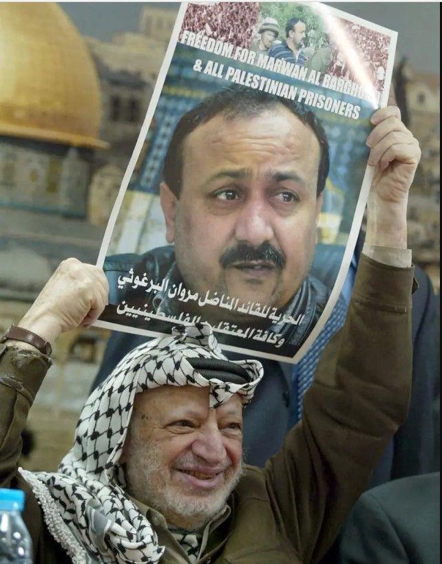الراحل القيادي الفلسطيني ياسر عرفات يحمل صورة مروان البرغوثي، ومكتوب عليها باللغة الإنجليزية الحرية لمروان البرغوثي، وخلفه صورة لقبة الصخرة.