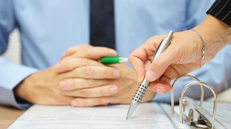 سيدة تكتب في ورقة أمام رجل جالس على مكتب
