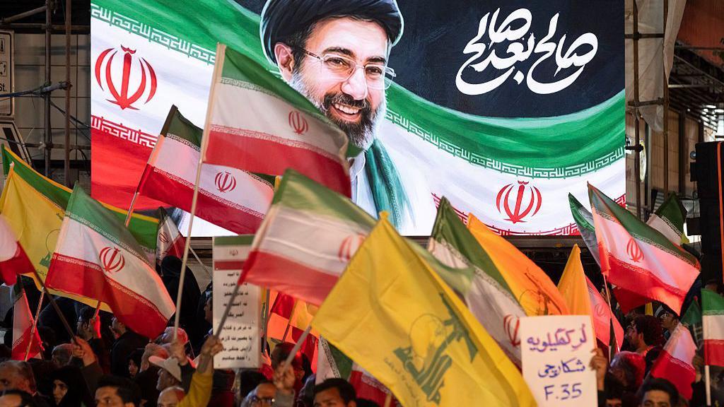 لوّح متظاهرون مؤيدون للحكومة الإيرانية بالأعلام الوطنية، وأعلام حزب الله اللبناني، ولافتة كُتب عليها بالفارسية: 